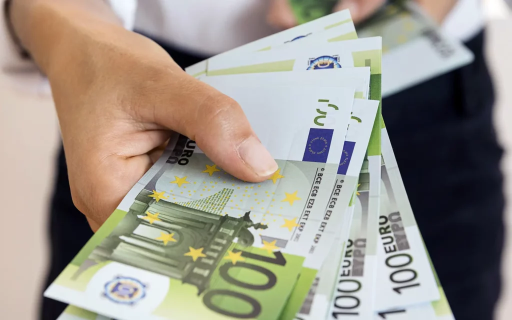 Plano focado nas mãos de uma pessoa a segurar e a contar várias notas de 100 euros em formato de leque.